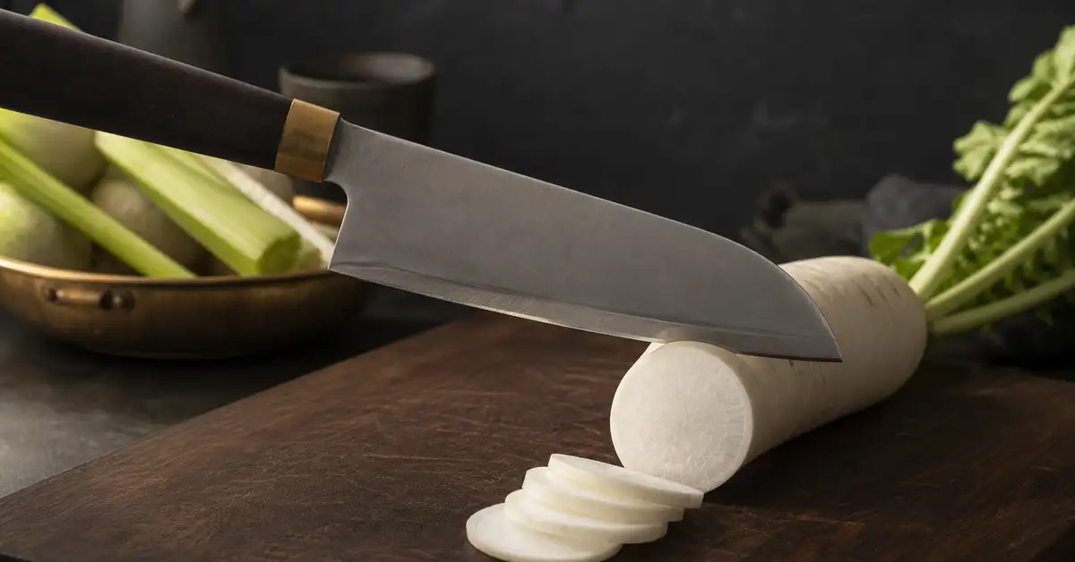 A Japanese-style santoku knife slicing cleanly through a vegetable on a wooden cutting board