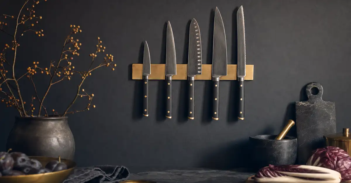 Kitchen knives stored on a wall-mounted magnetic strip above a slate counter