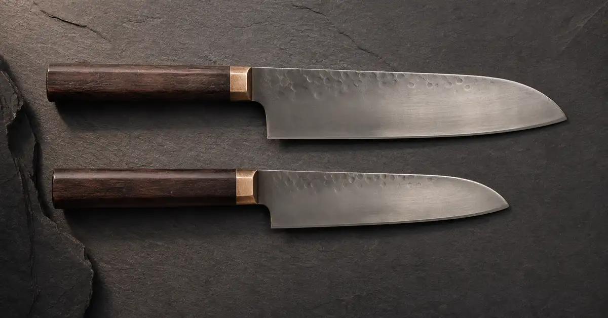 Two santoku knives of different sizes laid side by side on a slate surface